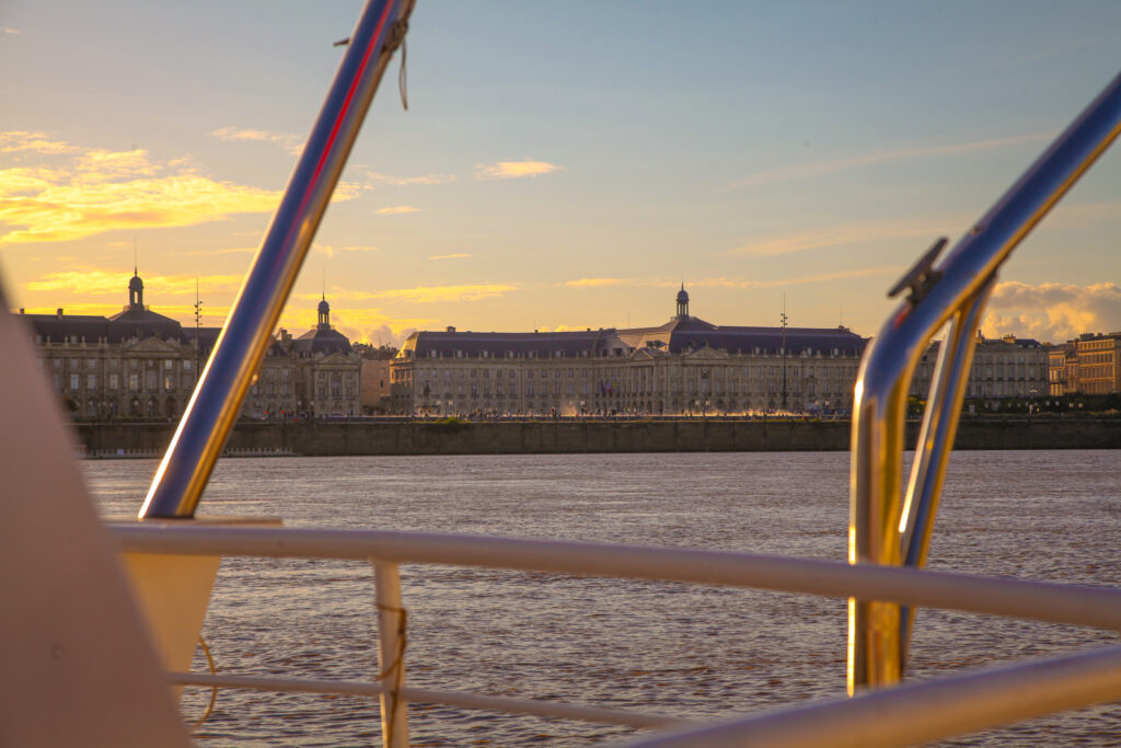 Vue depuis le ponton privé de Croisières Burdigala, avec la Place de la Bourse et le Miroir d'eau sublimée par le soleil couchant, mettant en valeur la beauté du paysage depuis l'Aquitania