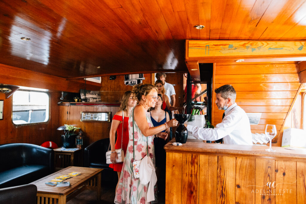 Un serveur derrière le bar du Burdigala 1, servant un verre à une dame qui vient d'arriver, lors d'un mariage à bord.