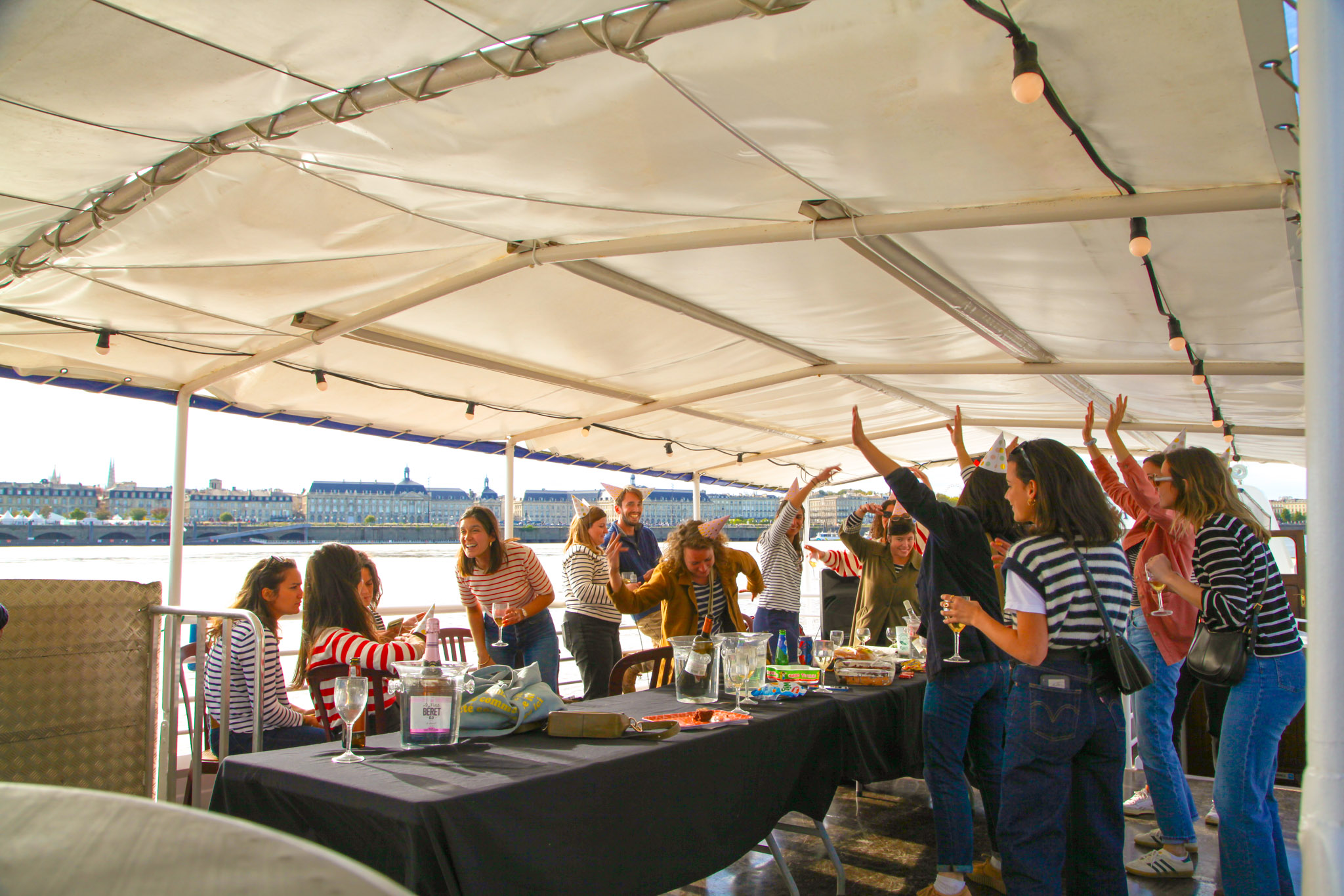 Fête d'anniversaire à bord du Burdigala 1, privatisé pour l'occasion. Les invités en marinière profitent de la croisière sur la Garonne avec la Place de la Bourse en arrière-plan.